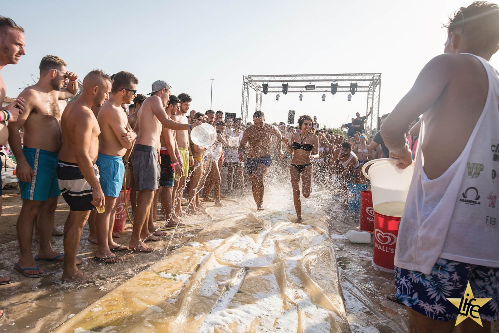 Juicy Event beach party - Deux participants de la beach party courant sur l'activité entourés de la foule qui les éclaboussent d'eau, à la soirée sur la plage.